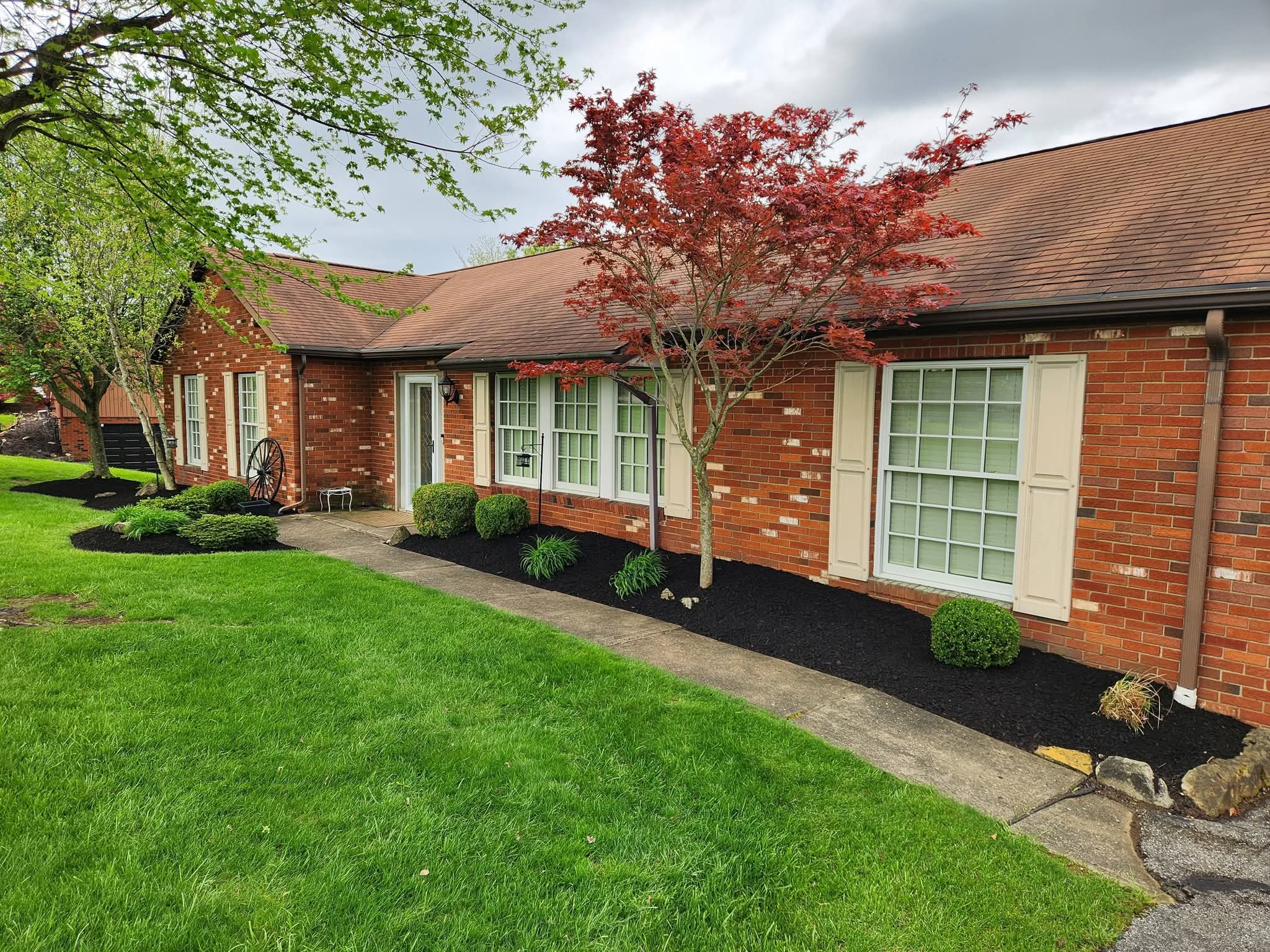 Brick ranch home with a green lawn and fresh black mulch beds along the walkway