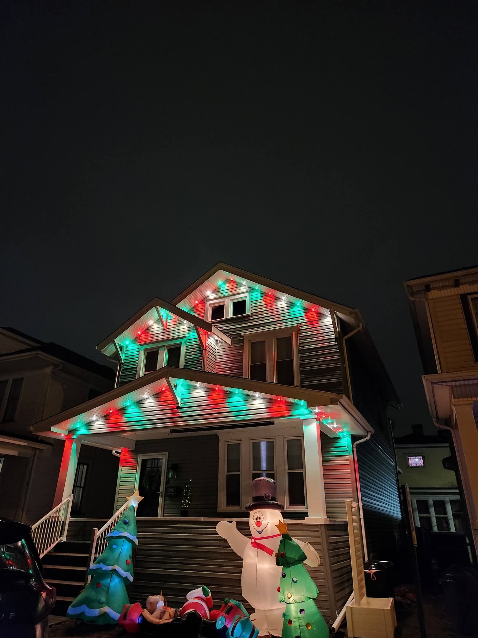 A two-story home with red, green and white lights along the porch and gables