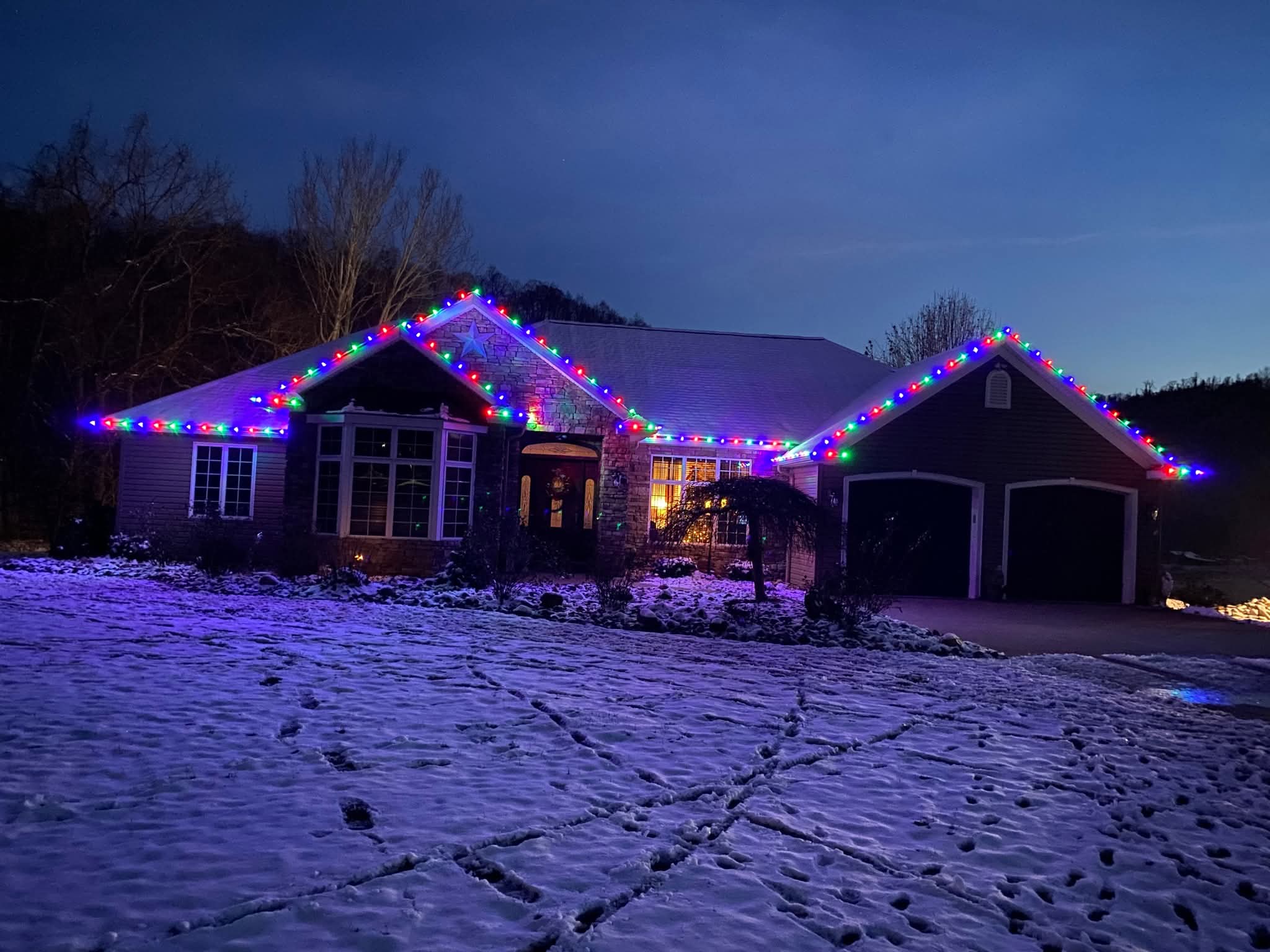 A home outlined in red, green, blue and white C9 lights on a snowy evening