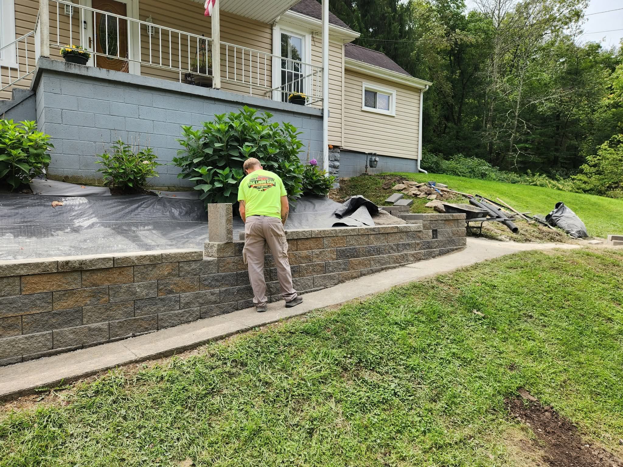 A K&K crew member building a block retaining wall in front of a house