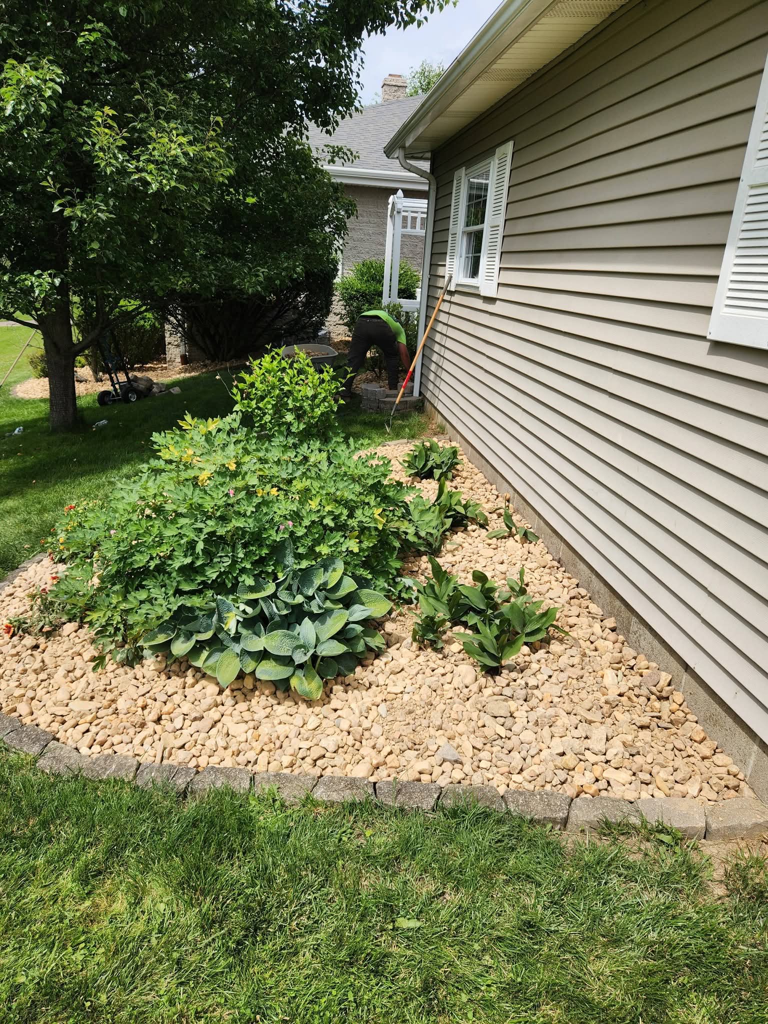 A crew member finishing a river rock bed with plants beside a house